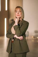 A woman in a green suit stands thoughtfully with hands on her chin