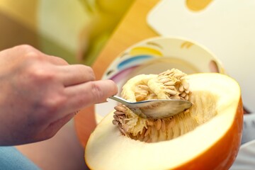 Removing seeds from a halved melon using a metal spoon, showcasing fresh fruit preparation technique