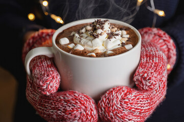 Warm cup of hot chocolate held in cozy mittens during winter season with soft lights in the background. Generative AI