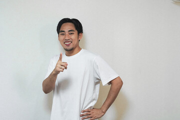 Smiling young man in a white t-shirt giving a thumbs up gesture.