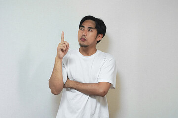 A thoughtful man in a white t-shirt, pointing upwards, considering something.