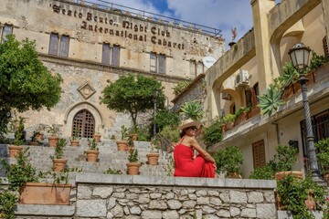 taormina, italien - frau in einem roten kleid mit hut vor einem alten palazzo - editorial