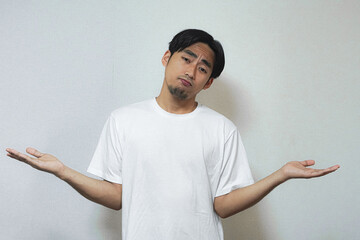 A young man in a white t-shirt shrugs, expressing uncertainty or indifference.