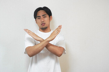 Young man in white t-shirt making a rejection gesture against a plain background.