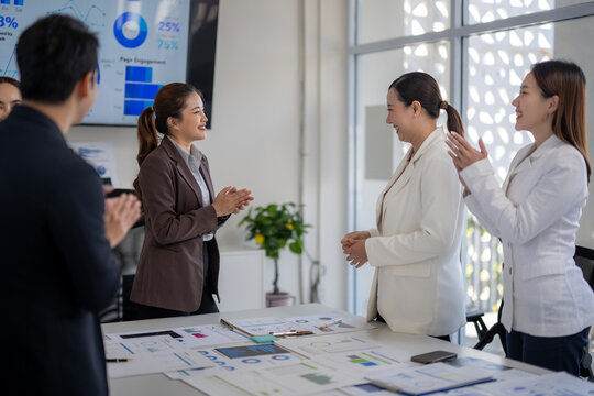 A group of people are standing around a table with a large monitor behind them