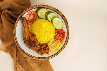 Top view of tumpeng, a cone-shaped Indonesian yellow rice dish, served with fried chicken, vegetables, tempeh, noodles, and sambal on a bamboo plate.