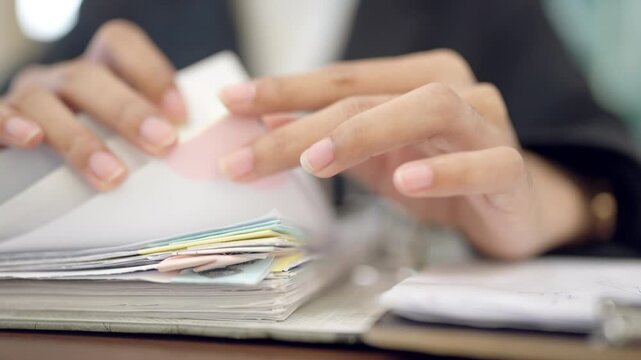 A person is looking at a stack of papers. The person is touching the papers with their fingers