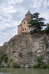 Fototapeta premium Ancient monastery perched on rocky cliff near a serene river under a cloudy sky