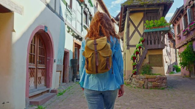 Woman with backpack walking on the beautiful street full of colorful houses with flowers of Eguisheim, France 