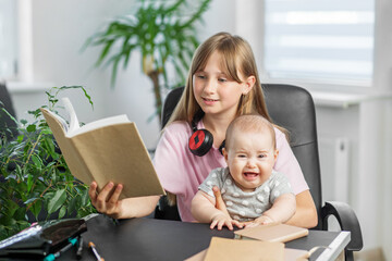 Baby crying while sister reads a book.