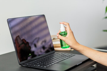Spraying laptop screen with green cleaning solution