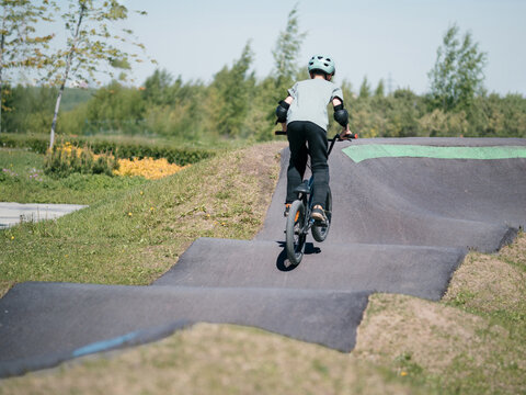 Child on bmx bike on pump track. Young male cyclist in helmet and protection rides bmx bike on asphalted bicycle race track. Boy BMX rider having fun and training on racing speed track. Extreme sport