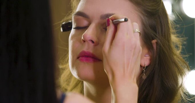Close-up video of a make up artist work in her beauty studio with client. Caucasian woman applying blusher on a client's face in a beauty studio. Slow motion 30 fps 4k footage.