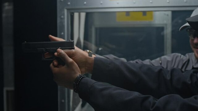 Side medium closeup of Caucasian male coach teaching black male law enforcement officer to hold and aim pistol, pointing at gunsights, while practicing at indoor shooting range