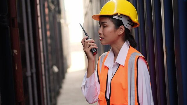 Portrait of Asian worker woman in safety uniform talking with walkie talkie to control work quality at container warehouse. working for logistic and shipping business.