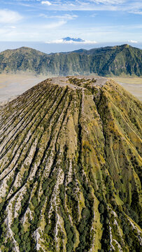 Aerial view of the majestic Mount Bromo Volcano, etched with deep valleys and colored in shades of green and brown against the sky, Mount Bromo Volcano, East Java, Indonesia.