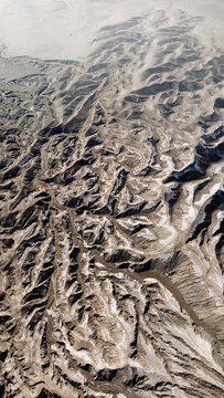 Aerial view of rugged terrain unfolds in a tapestry of earthy browns and pale whites, sculpted by wind and time near Mount Bromo Volcano, East Java, Indonesia.