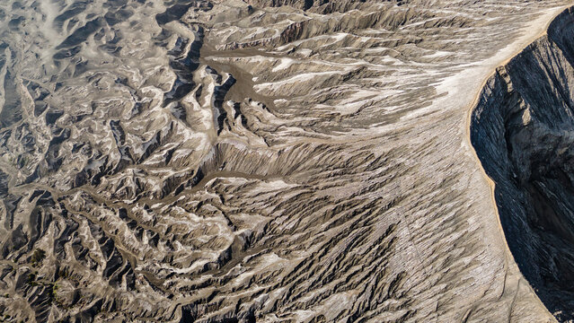 Aerial view of barren landscape sculpted by wind and time, etched with deep ravines and shadowed valleys, Mount Bromo Volcano, East Java, Indonesia.