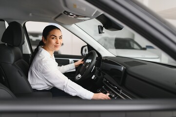 Beautiful girl looking through the car window. Business woman choosing new car in car dealership