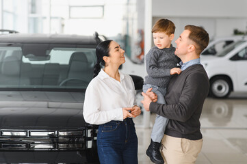 Young happy family enjoying while buying a new car in a showroom