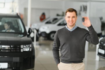 Handsome man customer holding key from auto, buying brand new car in showroom