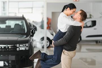 Beautiful young couple at car showroom exited because of buying a new car