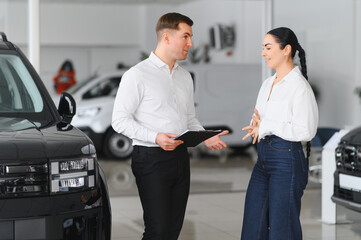 Young Caucasian woman buys a car at a dealership. Bearded man seller gives the car keys
