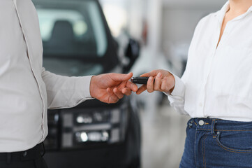 Young caucasian woman buys a car at a car dealership. Bearded man seller gives the car keys