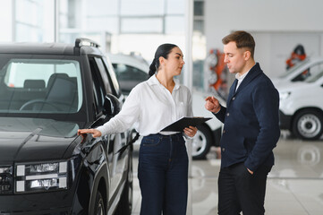 Friendly female car dealer standing at fancy car showroom and having consultations with a customer