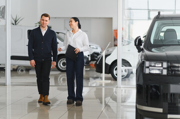 Young attractive woman salesperson in car showroom showing a car to her male client