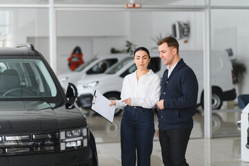 Friendly female car dealer standing at fancy car showroom and having consultations with a customer