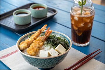 Japanese shrimp tempura rice bowl, miso soup and iced black tea, on a blue table