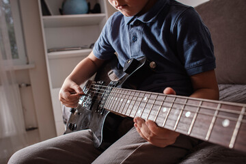Close-up of a child’s hand playing electric guitar. Focus on guitar strings and fretboard....