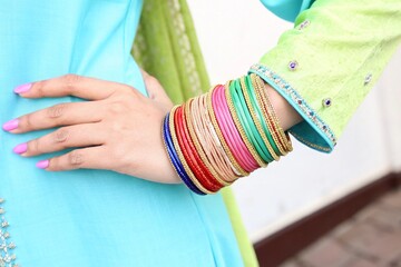 Woman's hand adorned with colorful bangles against a vibrant turquoise and lime green background design