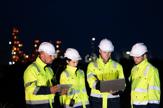 Group of engineer worker watching work monitor on laptop and checking for quality control at construction site of petroleum chemical industry or refinery oil plant factory overtime at night