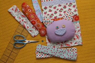 A soft textile toy cat, handmade, eyes made of buttons. Scissors and a ruler are lying next to the unfinished toy. Workflow. Top view.