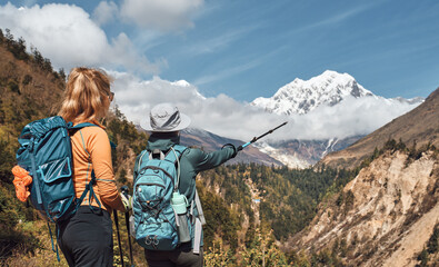 Women hikers with backpacks discuss hiking route against backdrop of beautiful Mansiri Himal range...