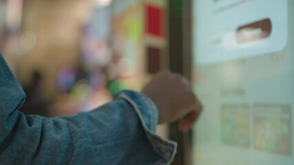 Close-up of hand pointing at menu on digital screen, selecting food options in self-service kiosk. Menu features food items like burgers and fries, with colorful buttons and interface visible