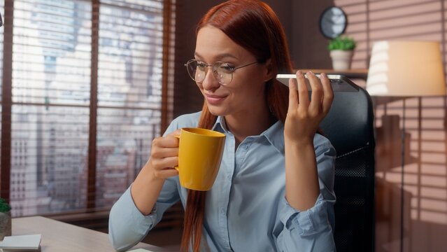 Caucasian woman businesswoman girl female business manager employer working pause break drinking tea coffee holding cup listening audio message voice mail with mobile phone at office smartphone listen