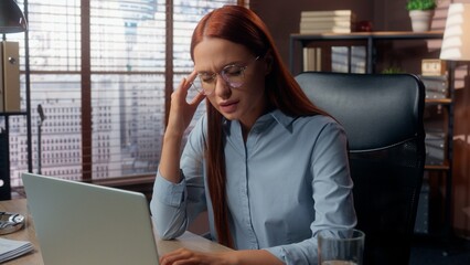 Caucasian business woman in office typing laptop feeling headache pain head tired overworked ill...