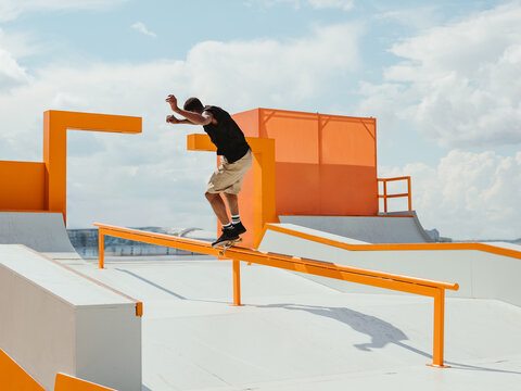 Latino Boy doing skateboard trick on rail in skatepark. Professional sportsman grinding on skateboard in park. Faceless unrecognizable young Latin skater doing Frontside 50-50 Grind trick on skate