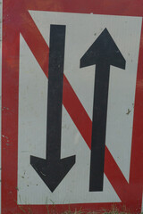 Two way traffic sign with red border and diagonal line, black arrows pointing up and down on white...