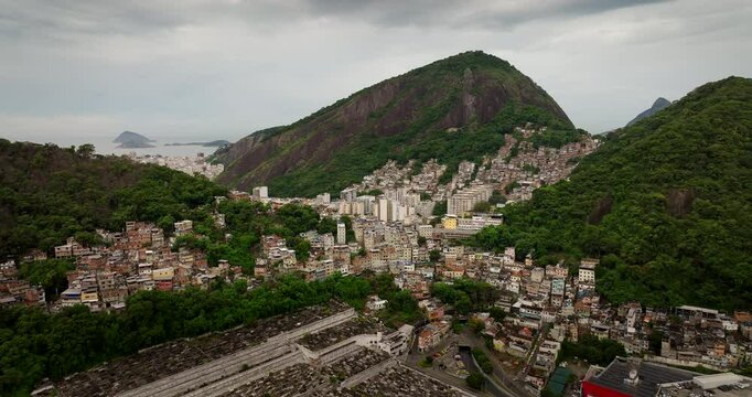 Sprawling favela on a green mountain overlooking S&atilde;o Jo&atilde;o Batista cemetery, Copacabana Bay in background, Social contrast in Rio de Janeiro, Brazil. Aerial forward