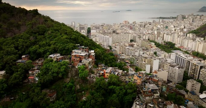 Aerial drone view of social inequality in Rio de Janeiro, dense favela on lush green hill contrasts with modern buildings of Copacabana. Brazil