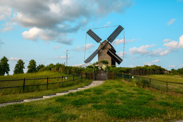 A picturesque scene featuring a historic windmill on a grassy hill under a bright blue sky. The...