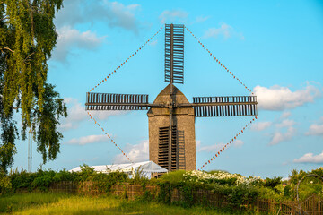 Vintage windmill with wooden blades set amidst beautiful countryside greenery and bright summer...