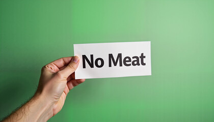 Hand holding "No Meat" sign against green background
