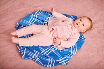 Young female child with light hair lying on blue checkered blanket. Dressed in pink, she appears...