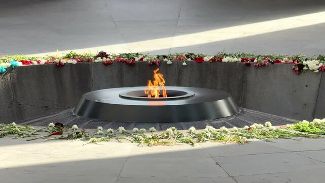A fire is burning in a small fire pit. Armenian Genocide Memorial Complex. The fire is surrounded by flowers
