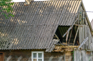 Damaged roof of an old wooden building covered with asbestos sheets, with broken structural...